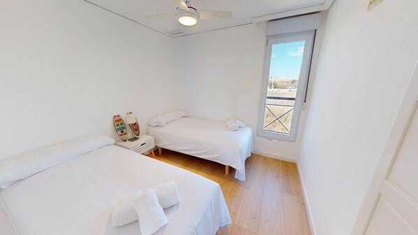 Une petite pièce lumineuse, avec deux lits, un ventilateur de plafond et une fenêtre donnant sur un beau paysage.