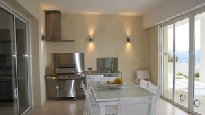 A modern kitchen with stainless steel appliances, a glass dining table, and a view of the outdoors. - Luxurious contemporary villa with magnificent sea view Nice, Alpes-Maritimes, France (Nice)