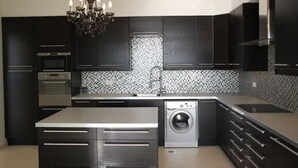 A modern kitchen with dark cabinetry, a stainless steel oven, a washing machine, and a chandelier. - Luxurious contemporary villa with magnificent sea view Nice, Alpes-Maritimes, France (Nice)