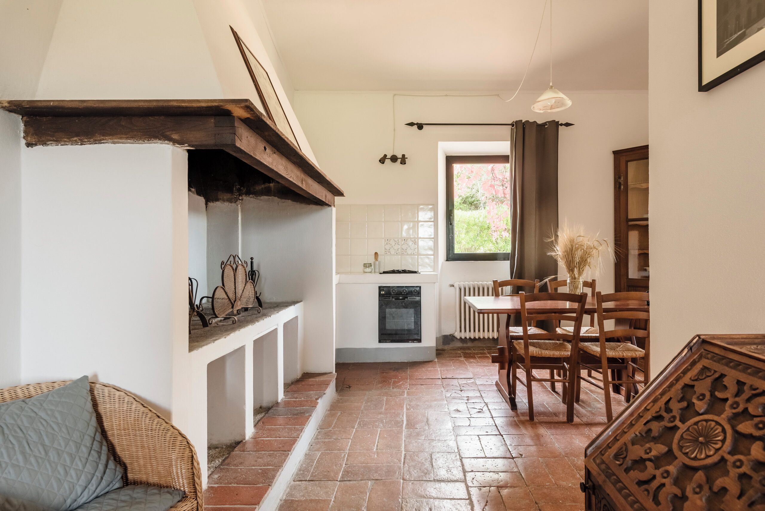 A cozy kitchen with a built-in oven, a dining area with wooden chairs, and a wicker sofa. - Studio on organic farm located in ancient hamlet.  (Monterotondo Marittimo)