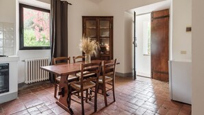 A dining area with a wooden table and chairs, a cabinet with glass doors, a radiator, and a window with curtains. - Studio on organic farm located in ancient hamlet.  (Monterotondo Marittimo)