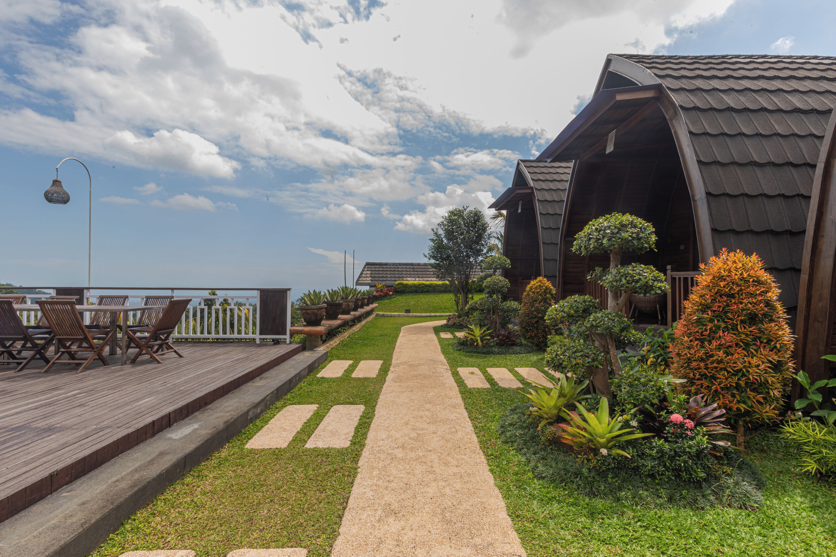 A wooden deck with outdoor furniture, a pathway, and a building with a sloped roof.