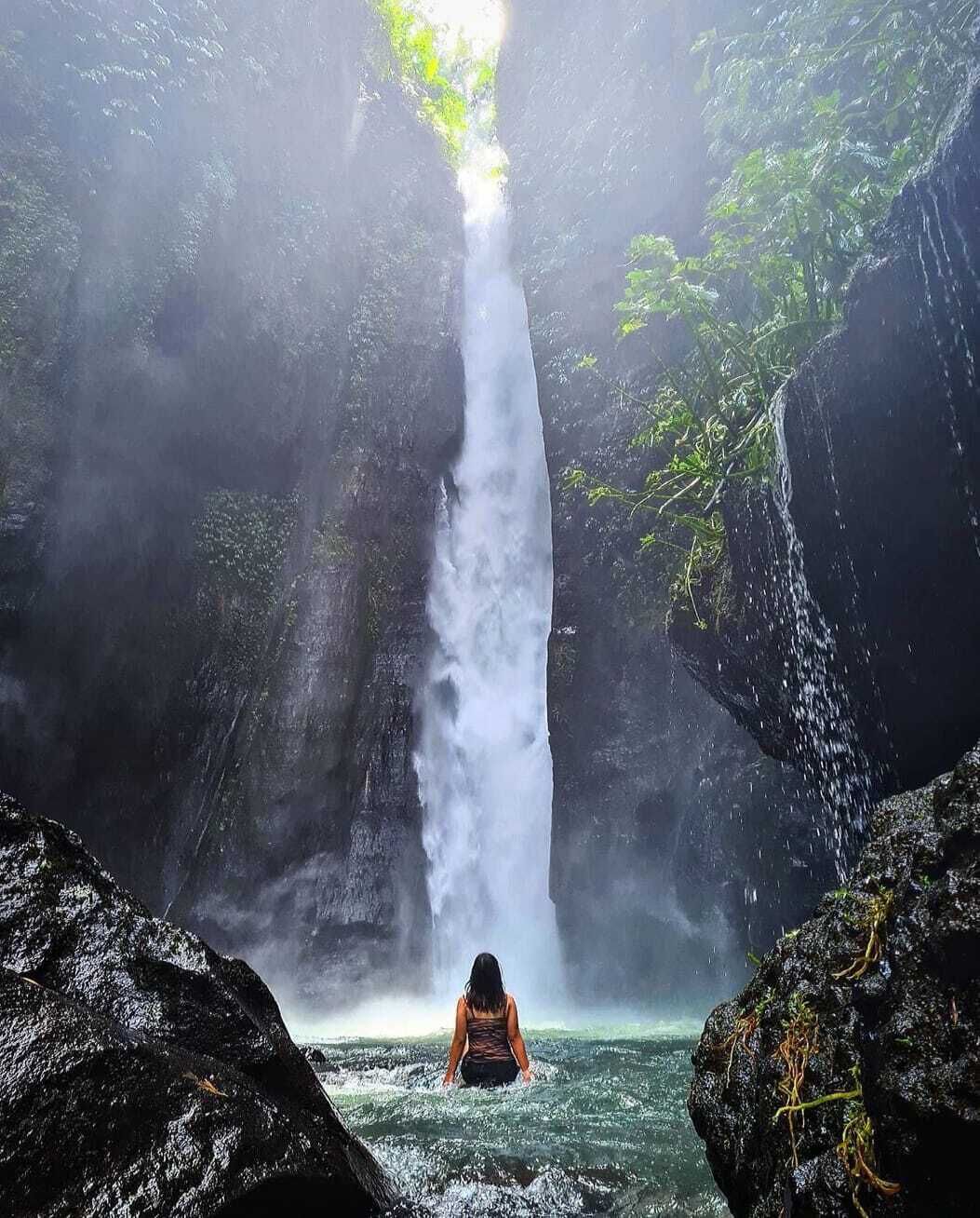 Una cascada en zona boscosa con una persona de pie en el agua.