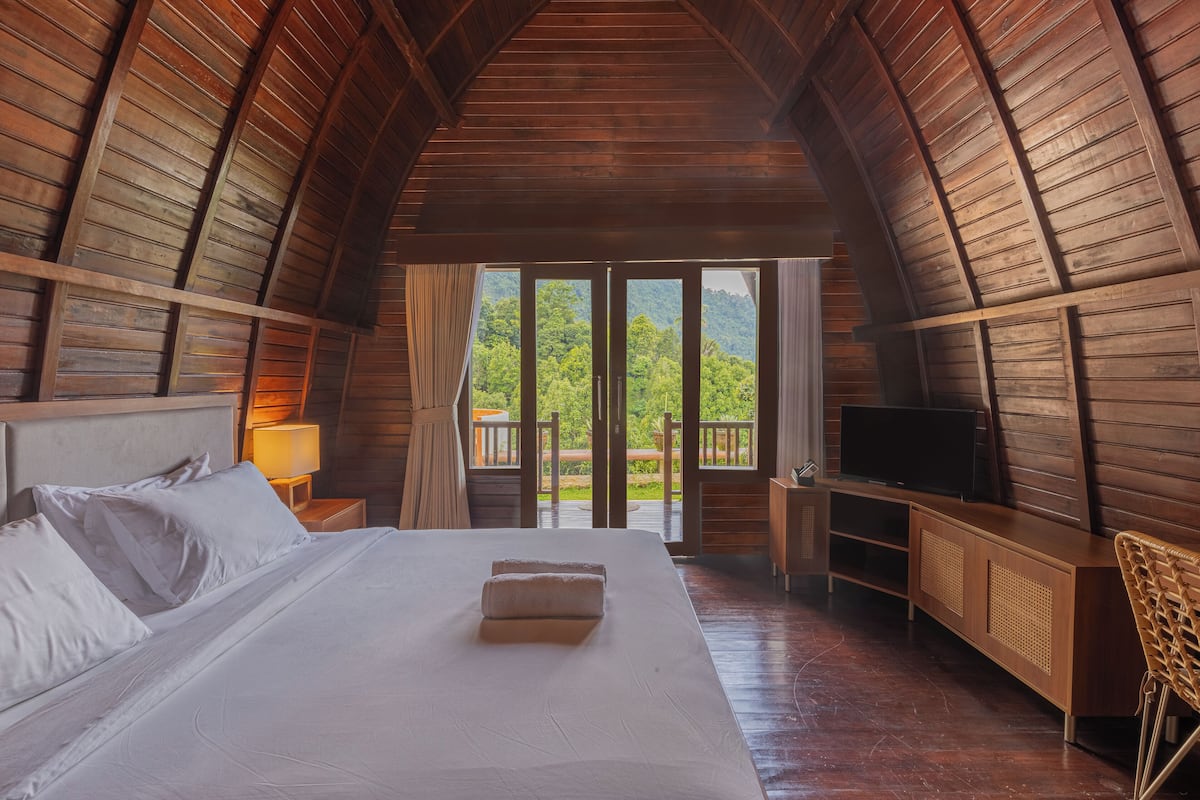 Un dormitorio con una cama grande, televisión y techo de madera.