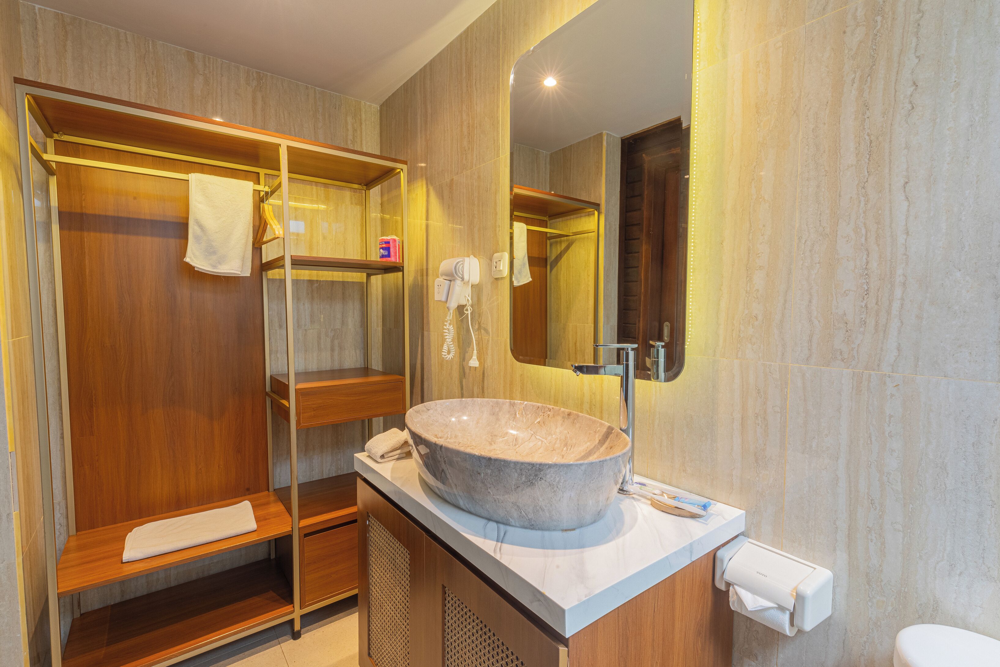 A bathroom with a large stone sink, wooden shelves, a towel rack, and a mirror.
