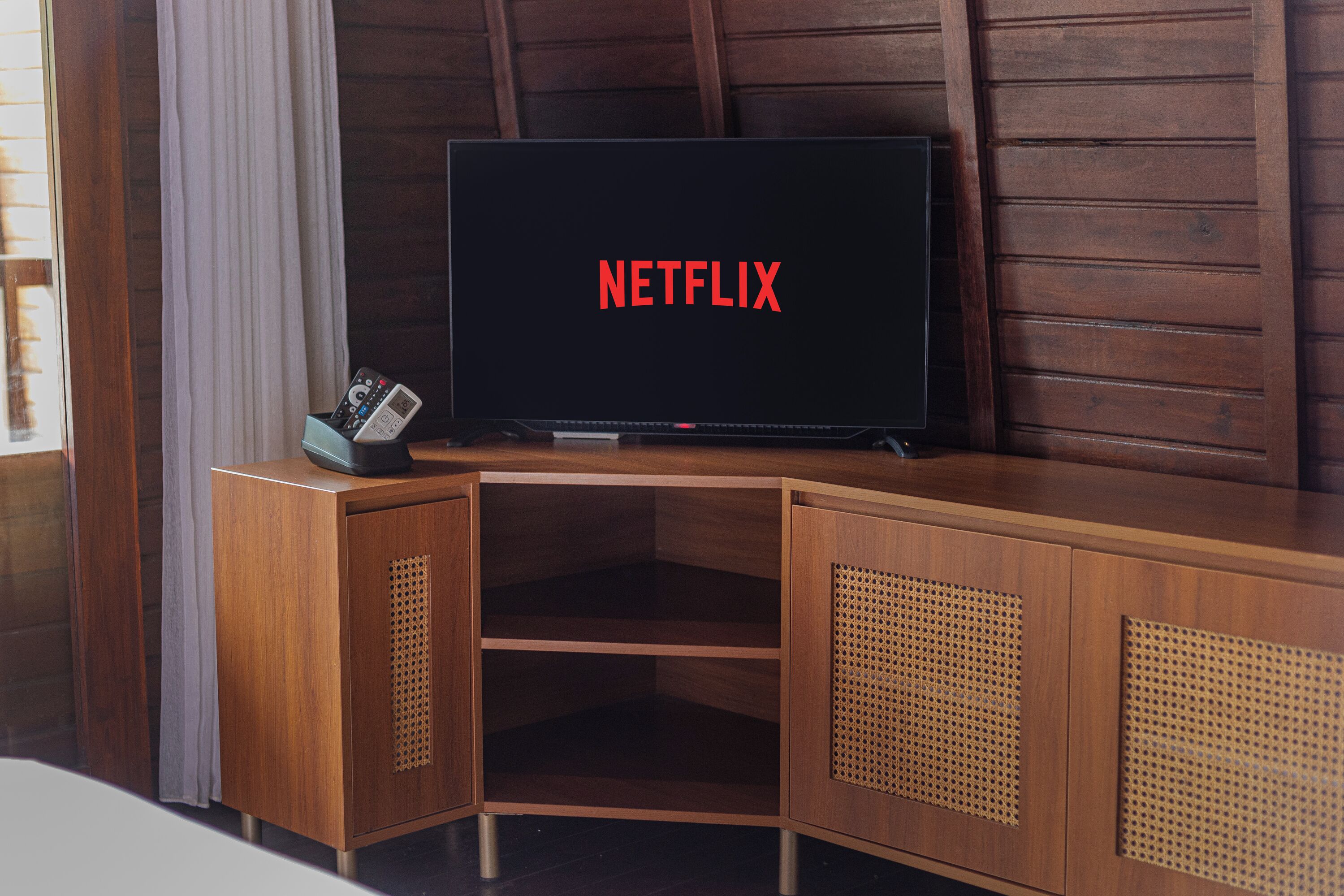 A wooden TV stand with a flat-screen TV displaying the Netflix logo, a remote control, and a small speaker.