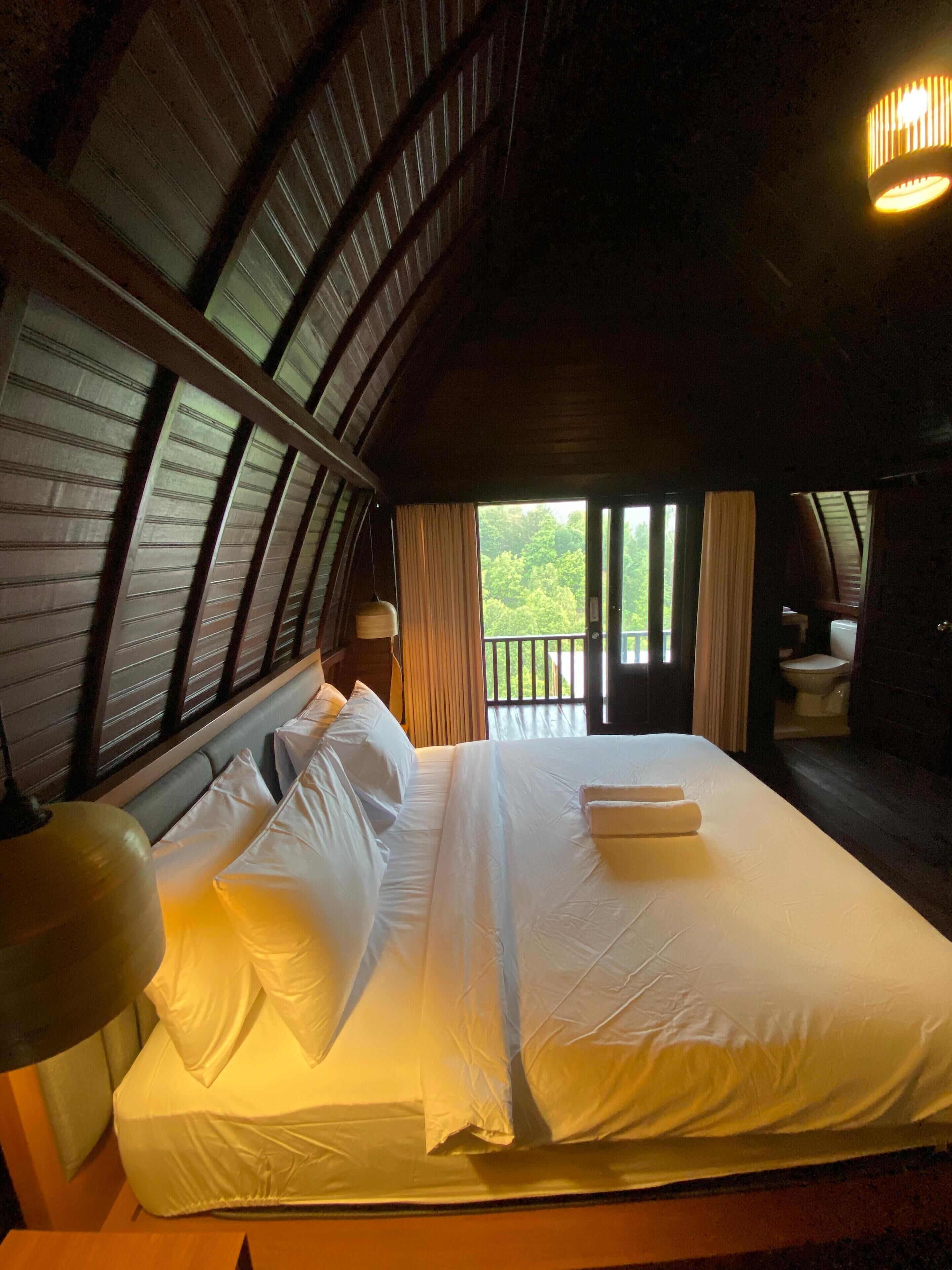 Ein Schlafzimmer mit einem großen Bett, Holzboden und Blick auf Grünlandschaft.