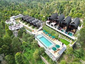 Vue aérienne d’un complexe hôtelier comprenant plusieurs hébergements de type bungalow, une piscine centrale et une végétation luxuriante environnante.