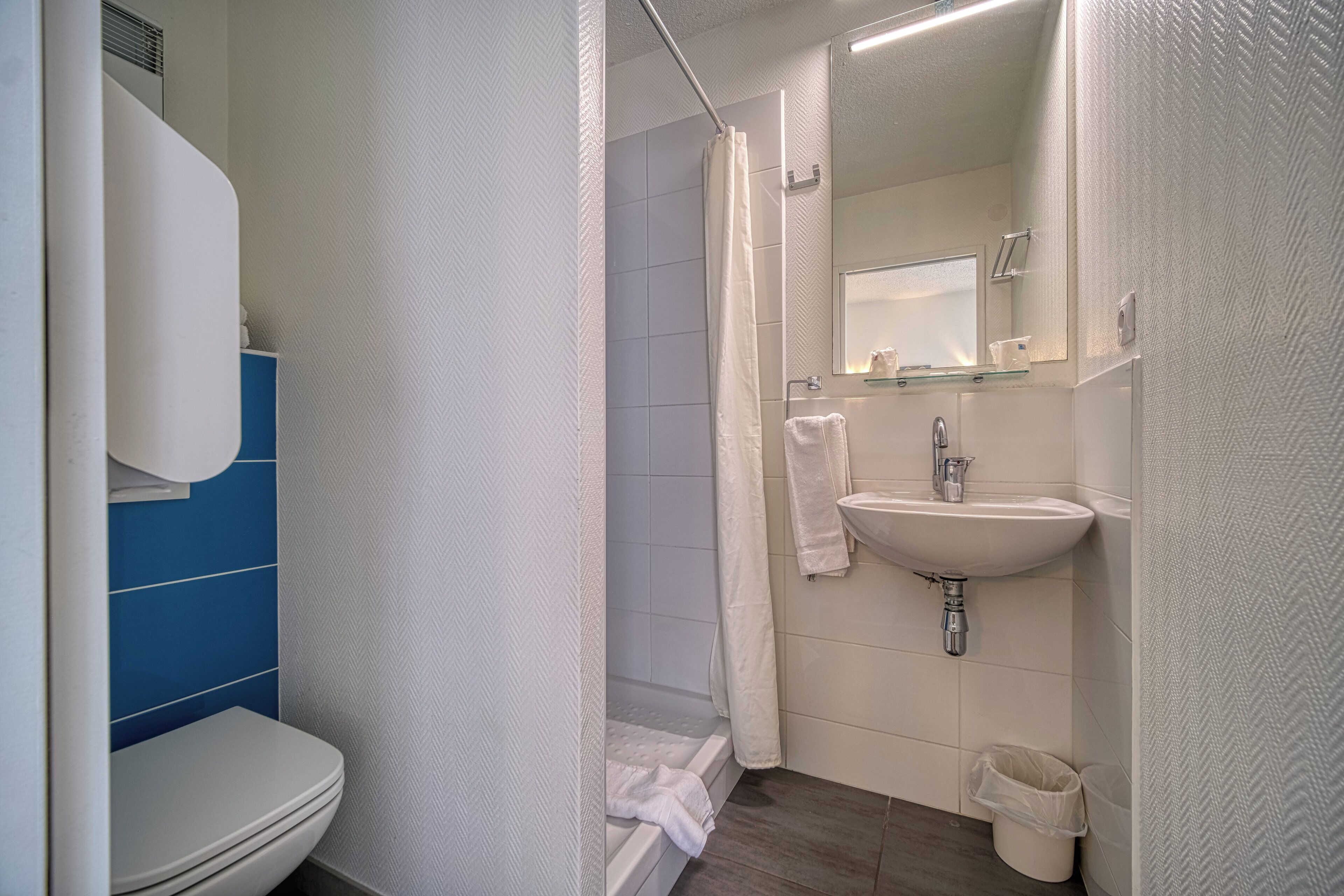 A bathroom with a toilet, shower, sink, and mirror.