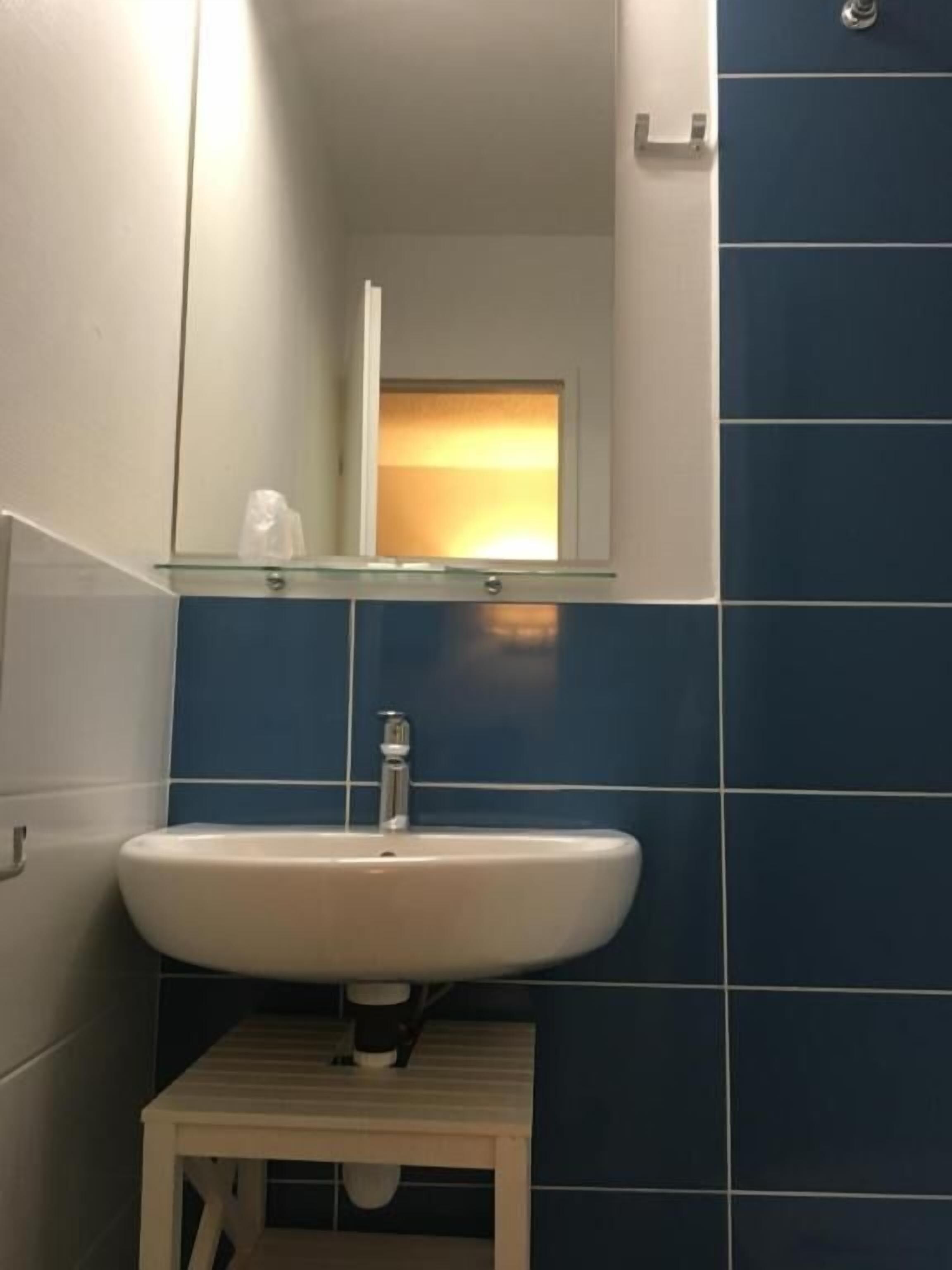 Ein Badezimmer mit weißem Waschbecken, einem Spiegel darüber und blauen Fliesenwänden.