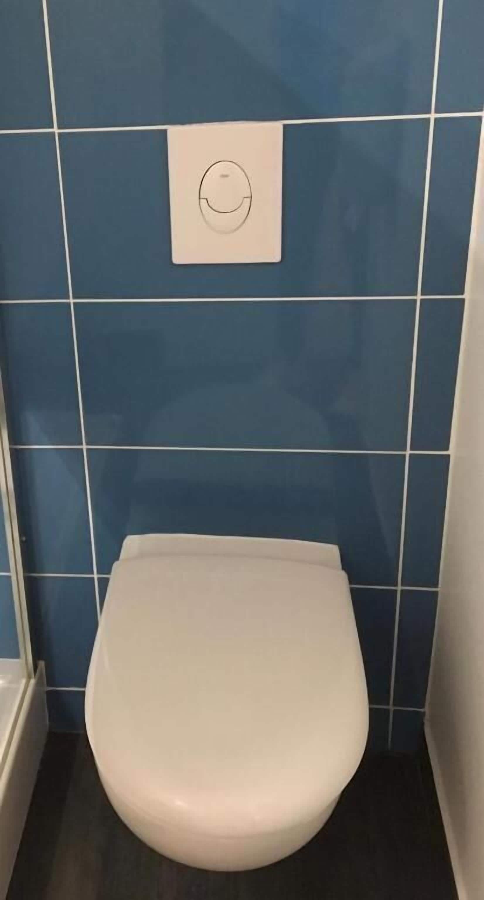 Eine kleine, weiße Toilette in einem Badezimmer mit blauen Fliesenwänden.