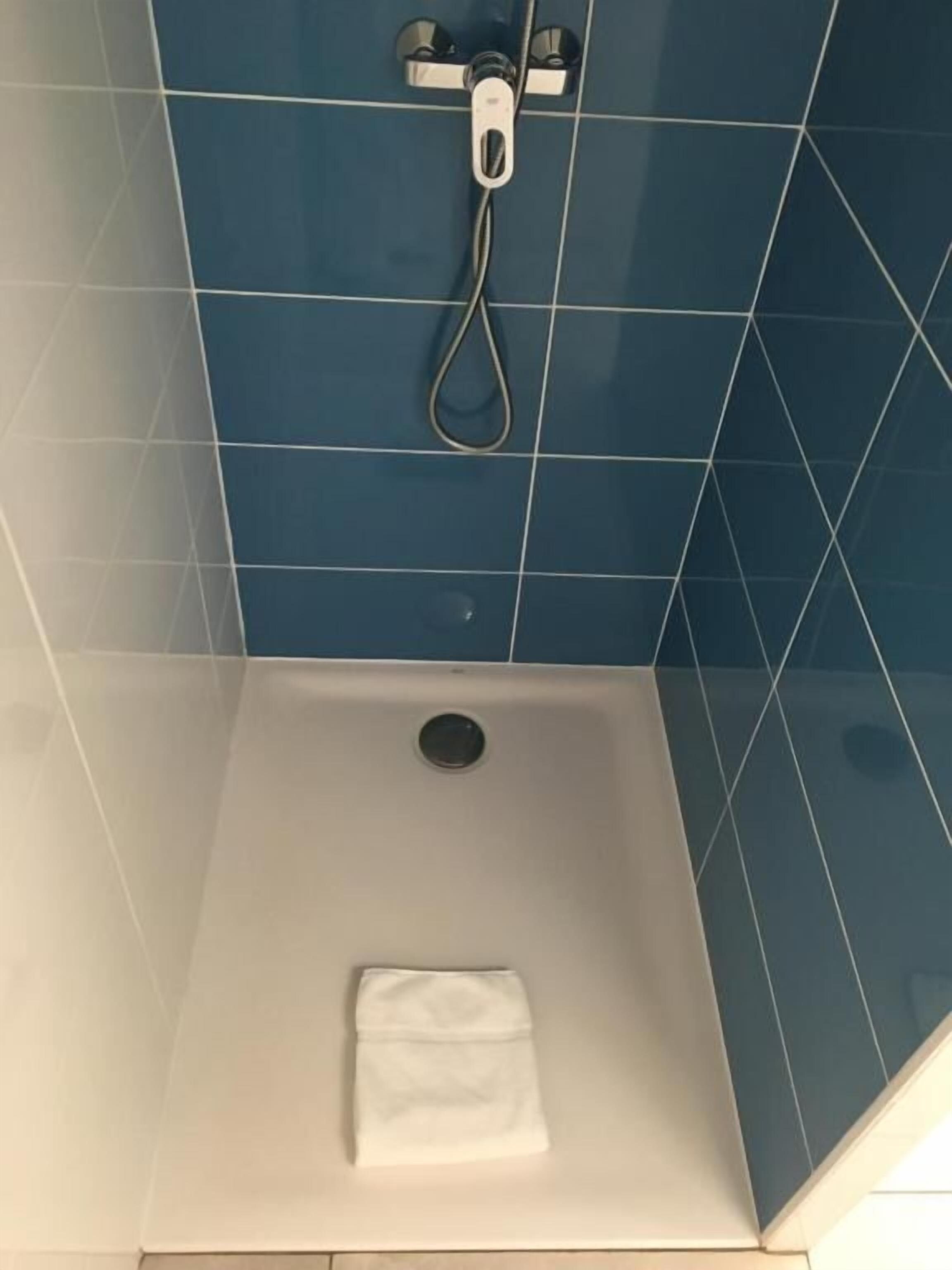 Une douche avec une serviette blanche sur le sol, des carreaux bleus sur les murs et un drain visible.