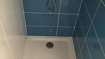 Une douche avec une serviette blanche sur le sol, des carreaux bleus sur les murs et un drain visible.