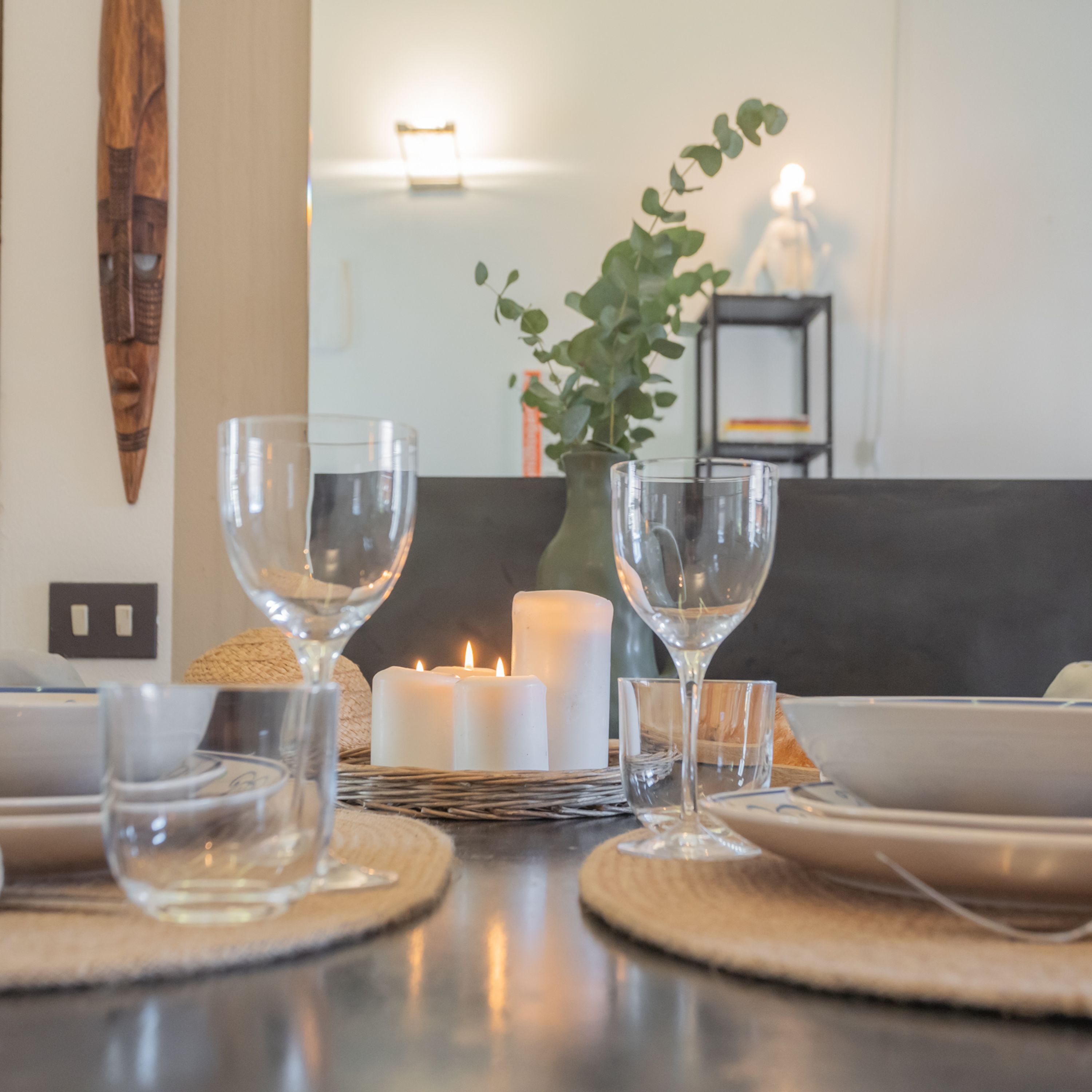 Una mesa de comedor dispuesta con cristalería transparente, una vela blanca y un protector de mesa tejido.