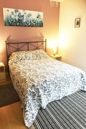 Un dormitorio con una cama, una mesita de noche, un cuadro colgado en la pared y una pequeña foto enmarcada.