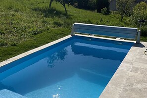 Piscina rectangular con borde de azulejos, rodeada de césped y árboles.