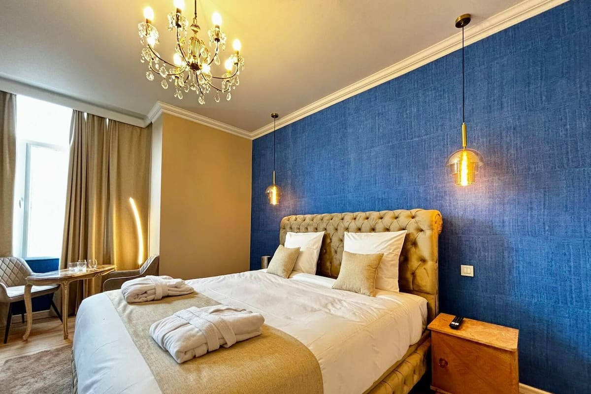 A hotel room with a large bed, a chandelier, a desk, and a chair.