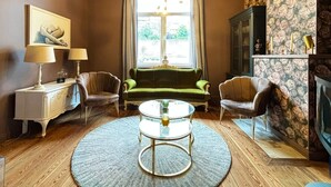 A living room with a green sofa, two armchairs, a glass coffee table, and a fireplace. - Maison du Roi (Liege)