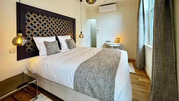 A modern hotel room with a large bed, two pendant lights, a small table, and a window with curtains. - Maison du Roi (Liege)