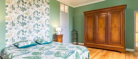 A bedroom with a bed, a wooden wardrobe, a nightstand, and a wall with a floral pattern.