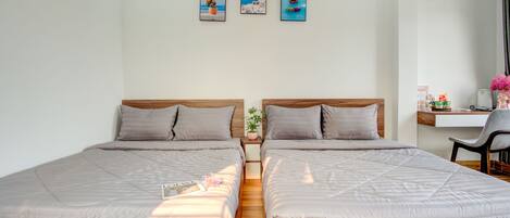 A double room with two beds, a small desk, and a chair. There are three framed pictures on the wall.