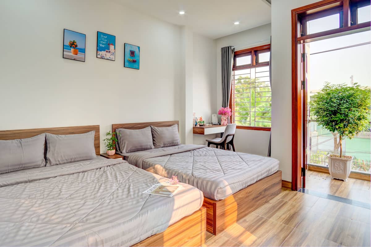 A hotel room with two beds, a desk, and a large window with a view of greenery.