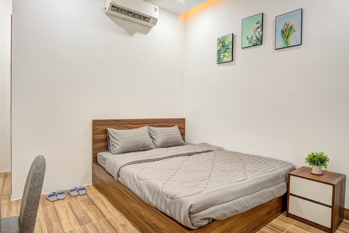 A bedroom with a wooden bed, a small bedside table with a plant, and a wall-mounted air conditioner.