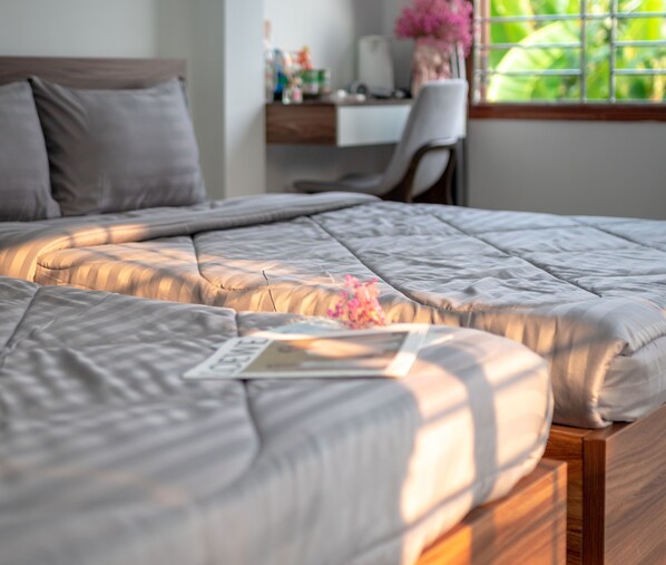 A neatly made bed with a pillow and a book, a desk with a chair, and a window with greenery outside.