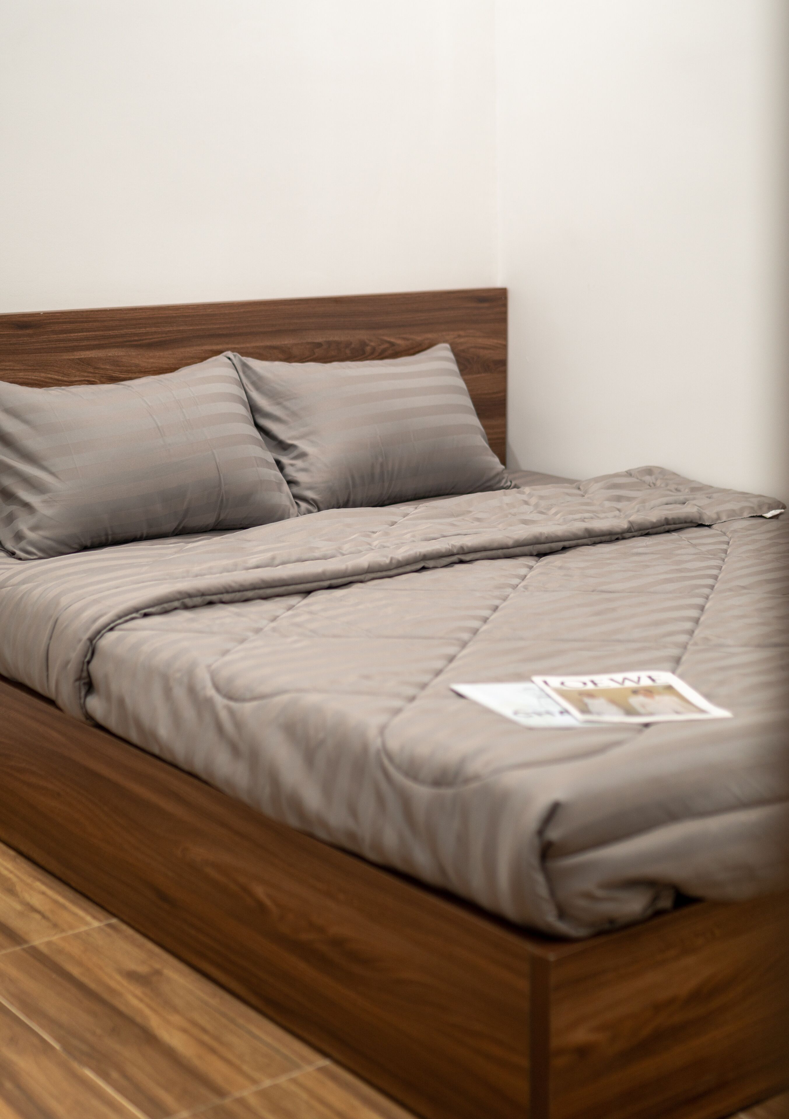 Uma cama com estrutura de madeira e colcha cinza.