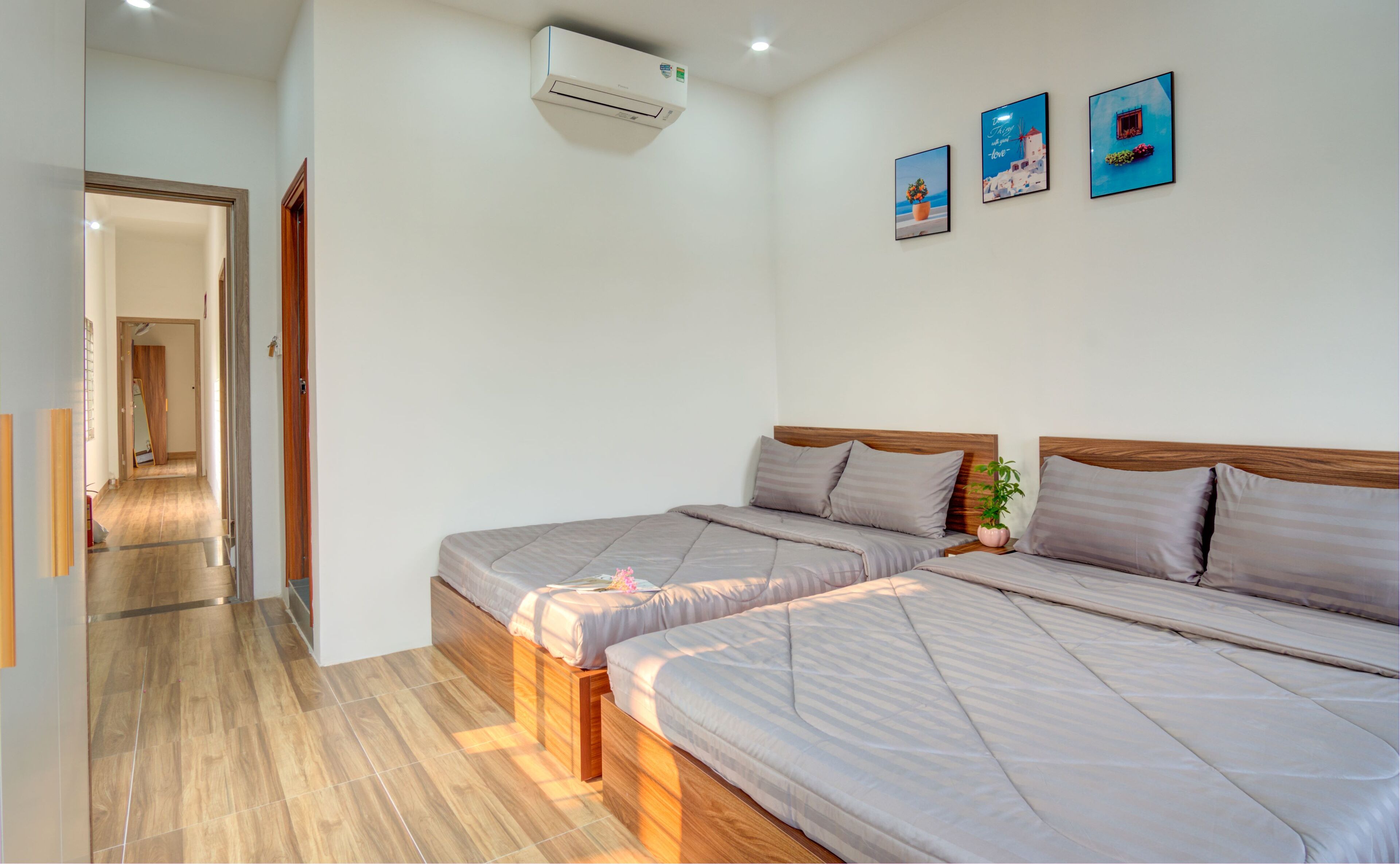 Ein Hotelzimmer mit zwei Betten, Holzboden, Flur und einer Wand-Klimaanlage.
