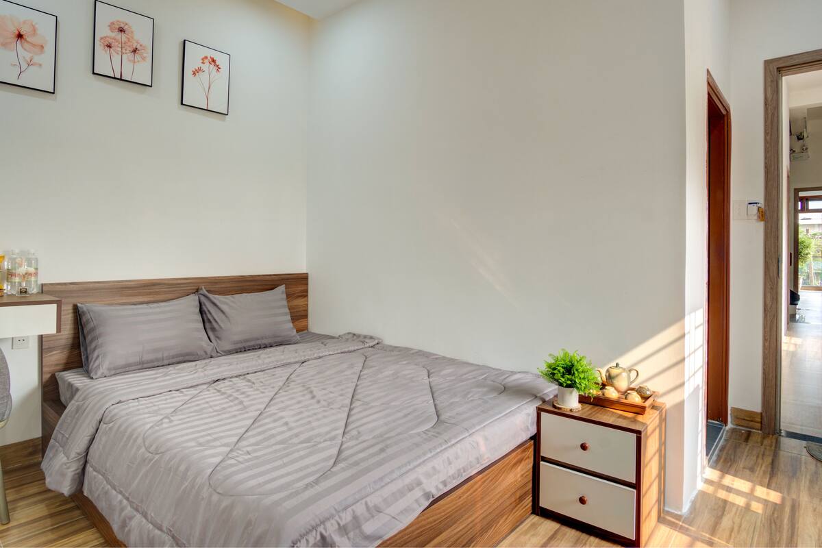 A bedroom with a bed, bedside table, and a nightstand with a plant and decorative items.