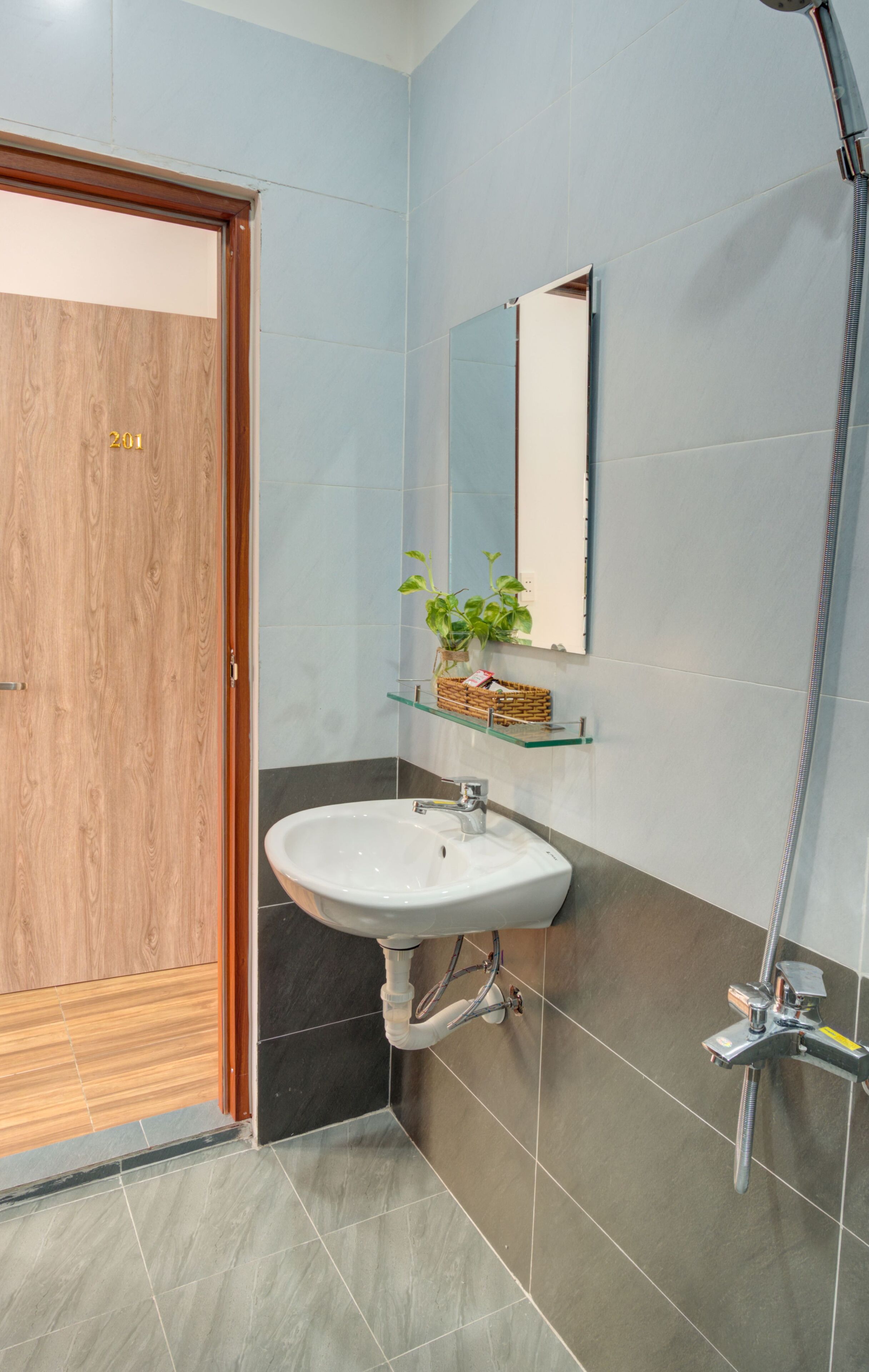 Ein Badezimmer mit Holztür, Waschbecken in Weiß, Spiegel und Dusche.