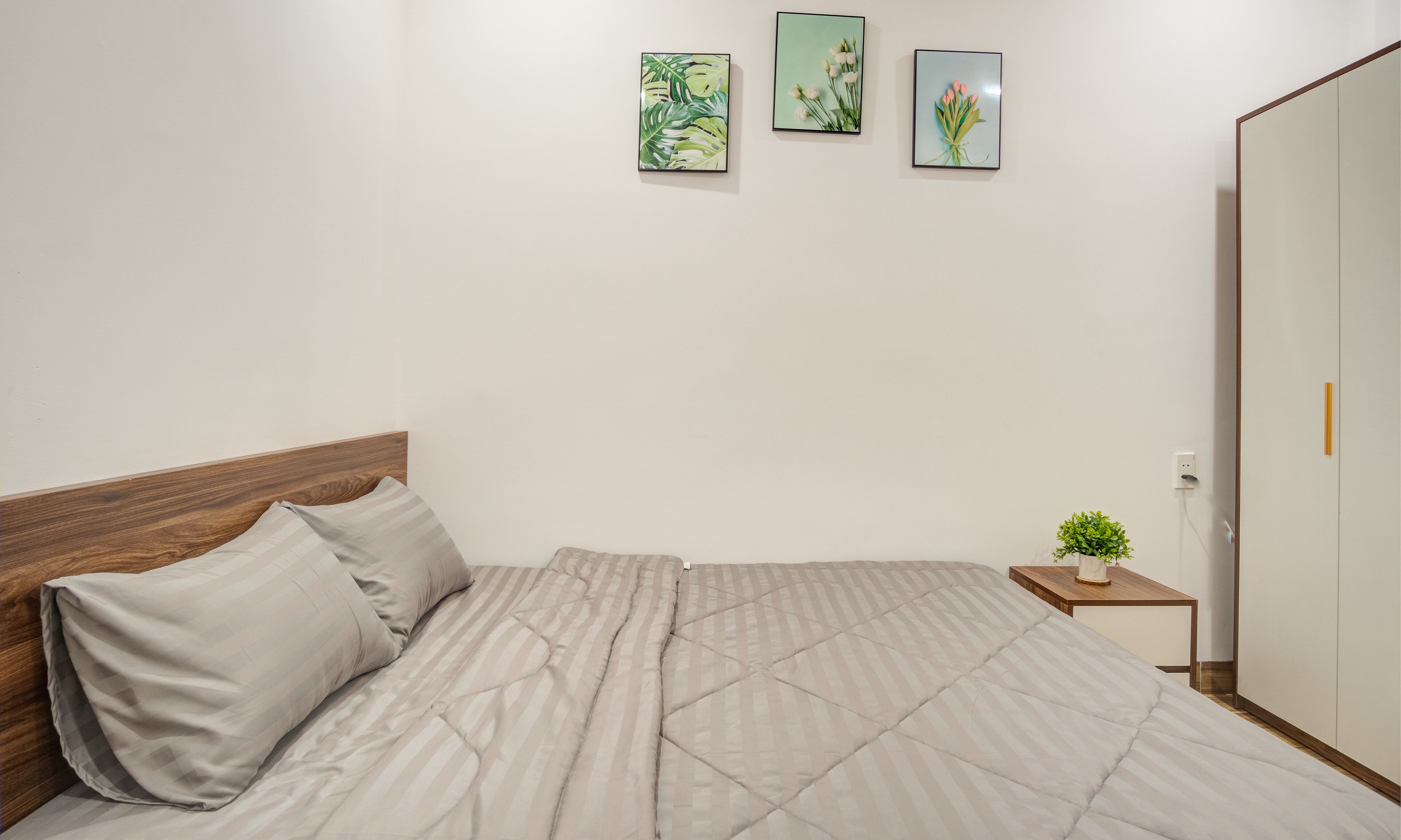 A neatly made bed with a striped duvet, a wooden headboard, and a small bedside table with a plant.
