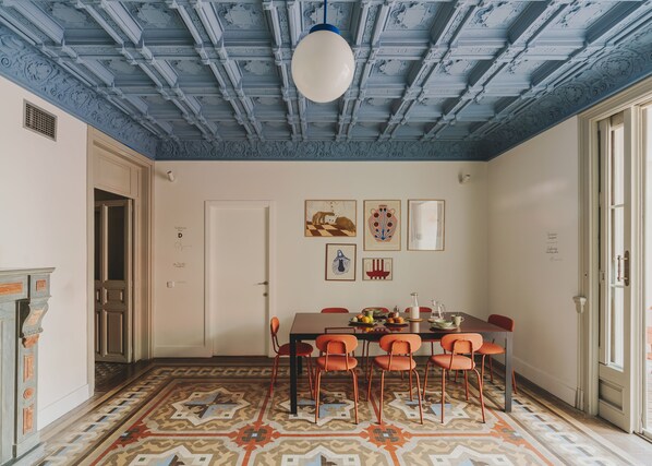 A dining area with a patterned floor, a table with chairs, and a ceiling with blue painted beams. - Piulet Hostel (Barcelona)