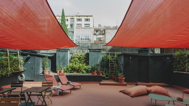 A rooftop terrace with red canopies, outdoor seating, and potted plants. - Piulet Hostel (Barcelona)