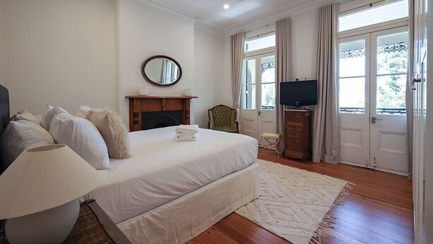 A bedroom with a bed, a television, a fireplace, and a view of the outdoors through the window.