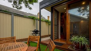 A patio with a wooden table and chairs, a grill, and a potted plant.
