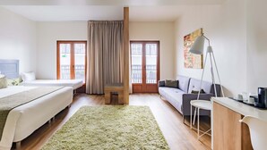 A hotel room with two beds, a sofa, a desk, a chair, and a green rug. - Porta da Arrábida Suites (Palmela)