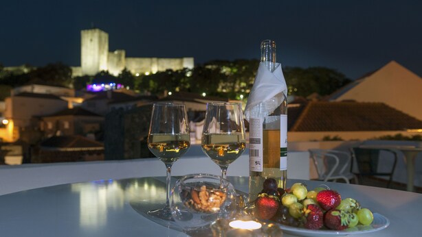 A table with two wine glasses, a bottle of wine, a plate of fruit, and a candle. - Porta da Arrábida Suites (Palmela)