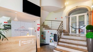 A hotel reception area with a wooden desk displaying "BEM-VINDO WELCOME" and a sign for "PORTA DA ARRÁBIDA HOSTEL & SUITES PALMEIRA". - Porta da Arrábida Suites (Palmela)
