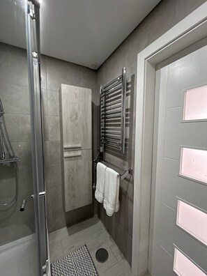 A modern bathroom with a glass shower enclosure, a wooden cabinet, a towel rack, and a door with a frosted panel. - Ammo Casa Terraço (Olhão)