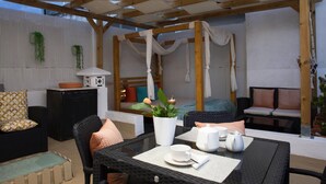 En uteplats med ett bord dukat för middag, en soffa och en säng med ett överhängande tygstycke.
