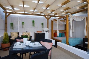A covered outdoor seating area with a table set for two, a sofa, and a bed with a canopy. - Ammo Casa Terraço (Olhão)