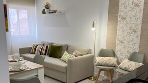 Ett modernt vardagsrum med en soffa, ett matbord och stolar. Här finns också en köksdel med en svart bänkskiva och ett handfat.