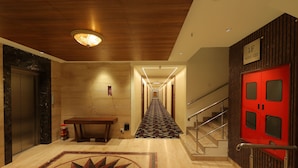 A hotel hallway with a wooden ceiling, a red door, a marble floor, and a patterned carpet. - Icon Grand Hotel by Bhagini (Bengaluru)