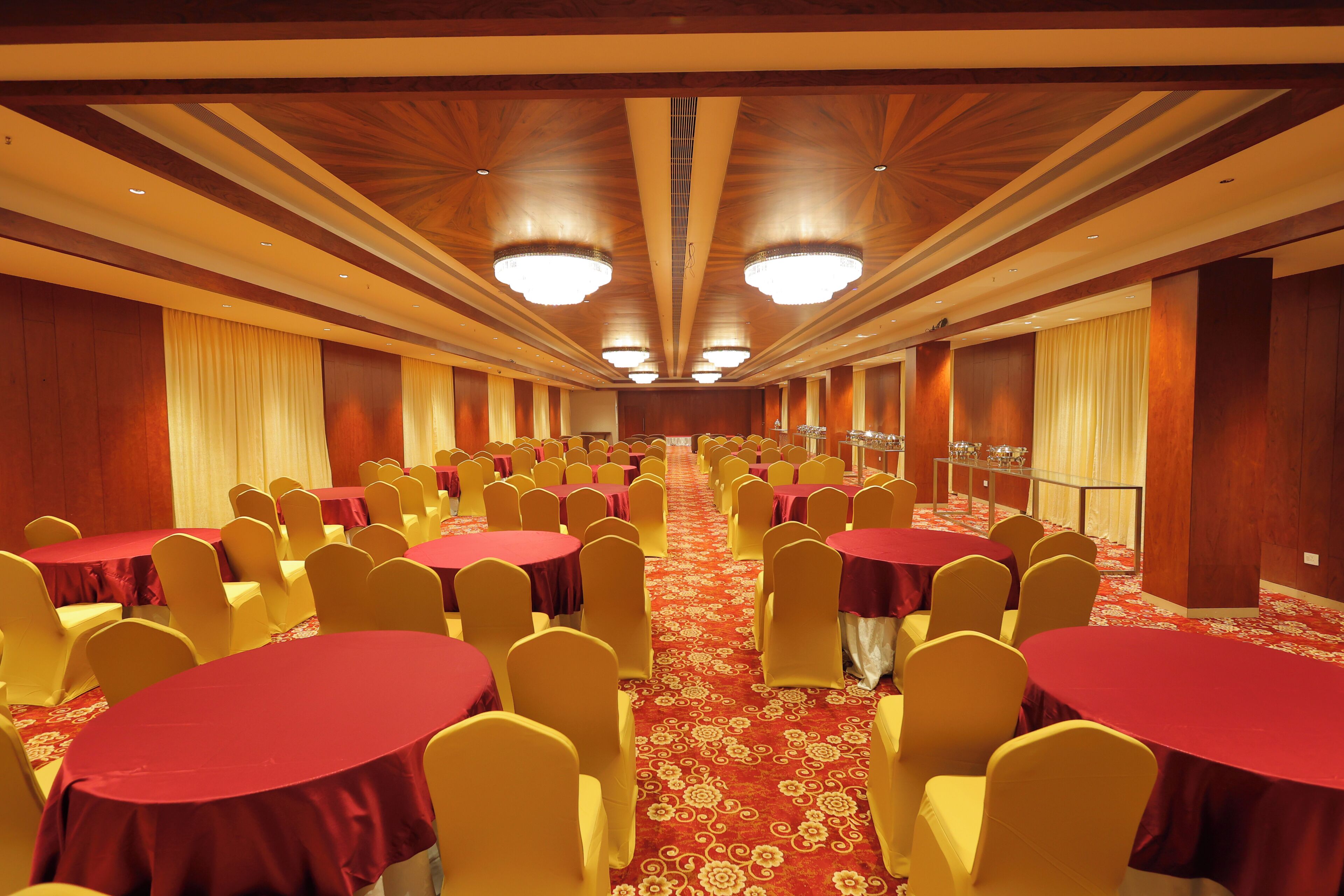 A banquet hall with rows of round tables and yellow chairs, a red carpet, and wooden paneling on the walls.