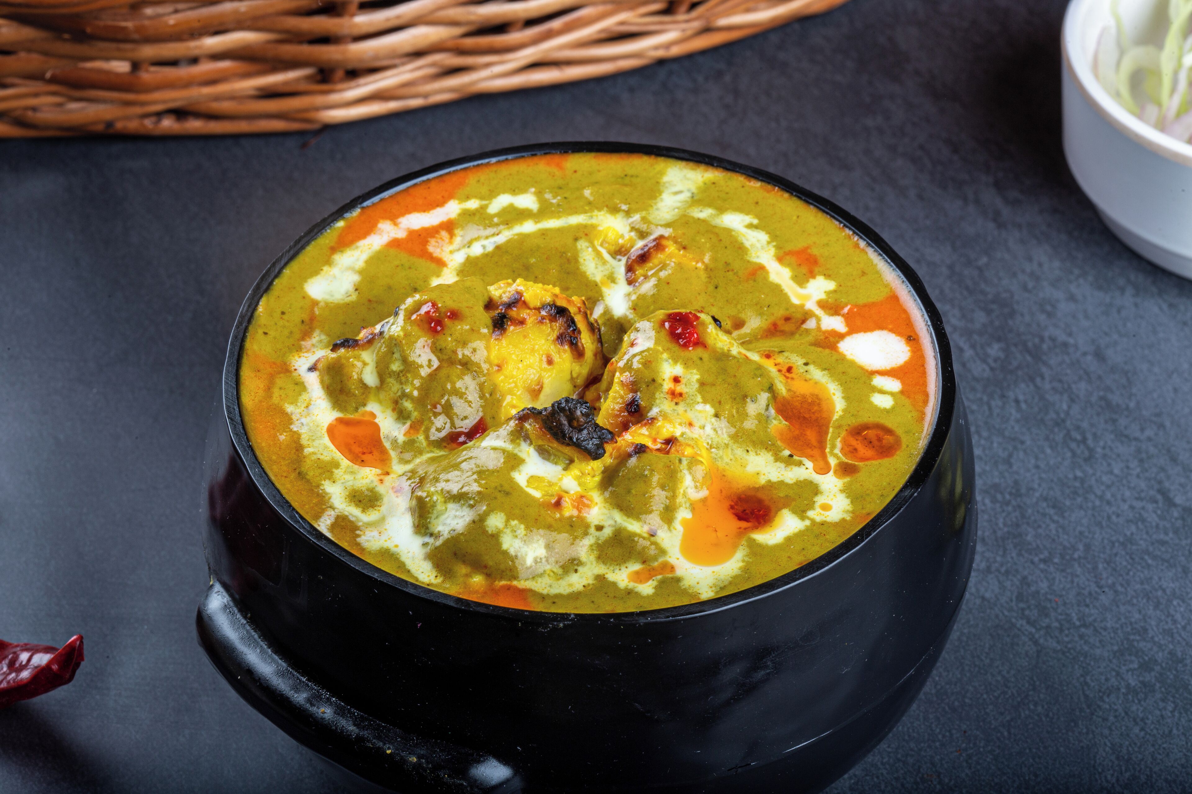 A bowl of curry with visible spices and a red chili on the side.