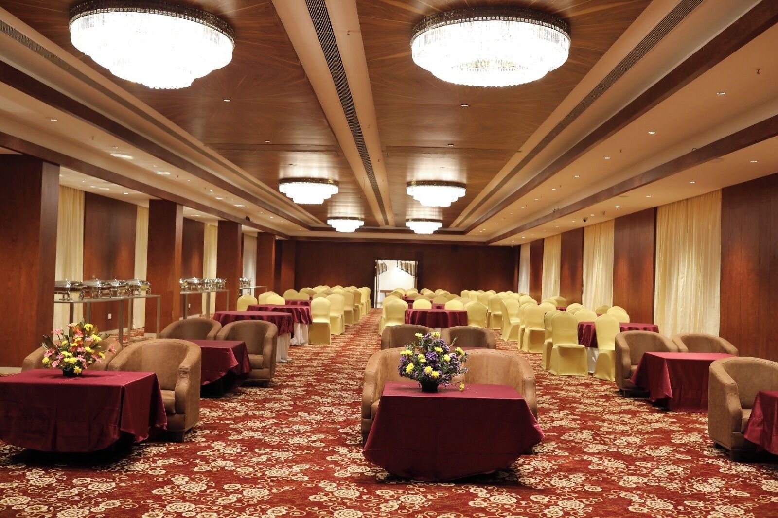 A banquet hall with rows of tables and chairs, chandeliers, and a carpeted floor.