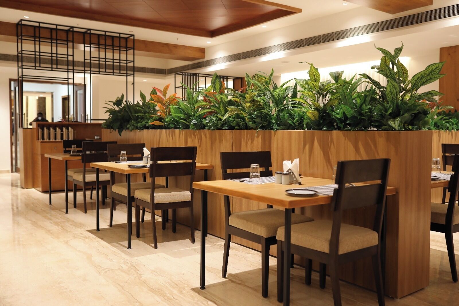 A restaurant with wooden tables and chairs, a high ceiling with wooden beams, and a green plant wall.