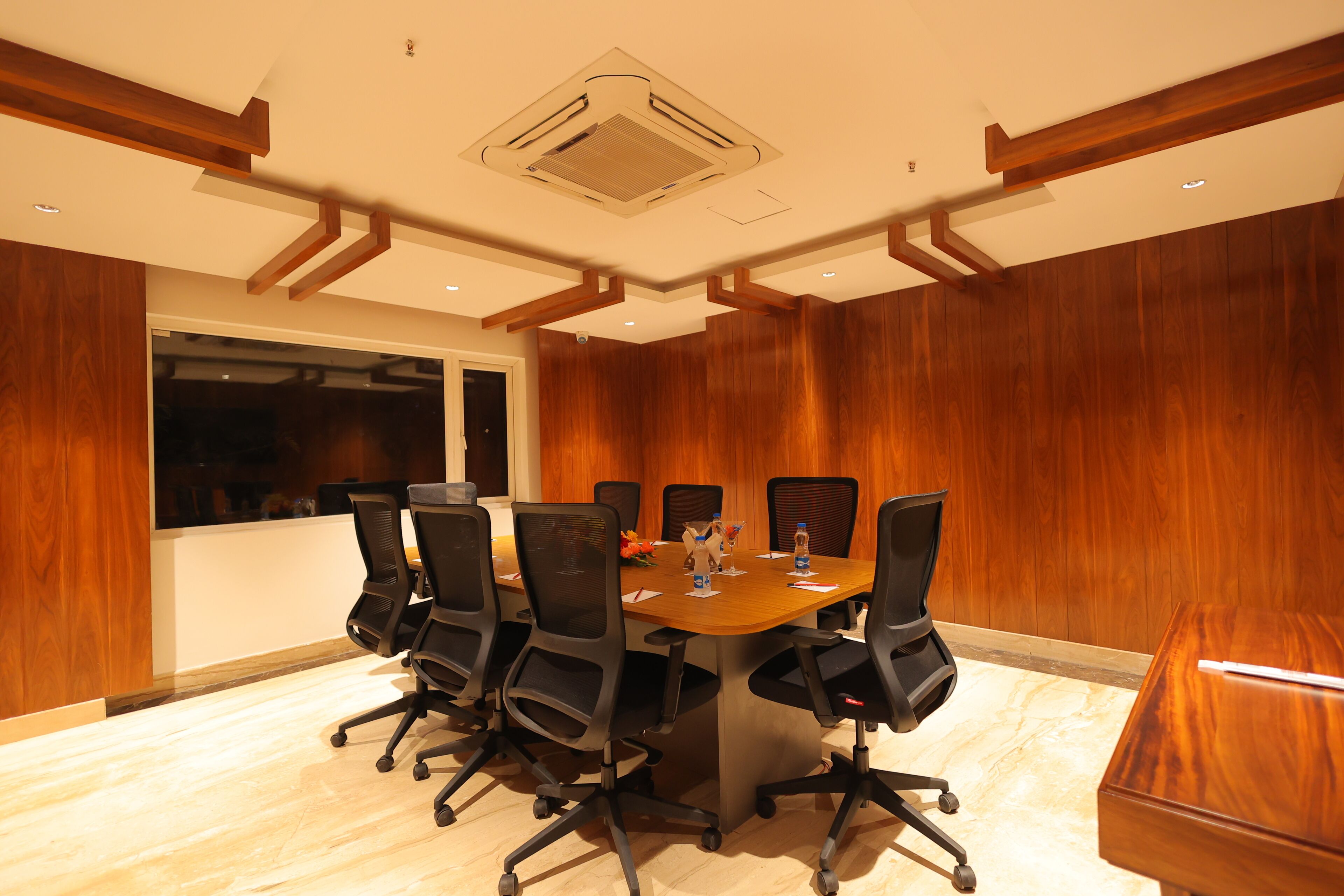 A conference room with a wooden table, black chairs, and a large window.